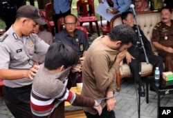 FILE - A police officer escort two men convicted of gay sex to be publicly caned at a mosque in Banda Aceh, Aceh province Indonesia, May 23, 2017.