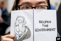 A furloughed government worker affected by the shutdown holds a sign that reads "Reopen the Government" during a silent protest against the ongoing partial government shutdown on Capitol Hill in Washington, Jan. 23, 2019.
