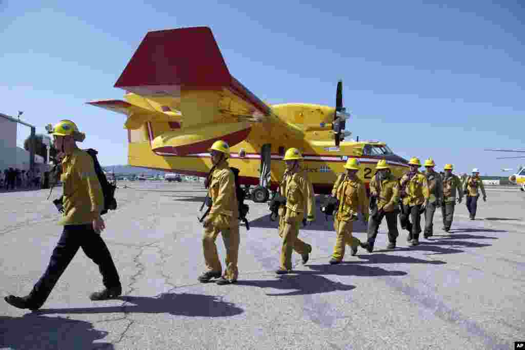 Los Angeles County firefighters walk past two Bombardier CL-415 Super Scooper firefighting planes parked at Van Nuys Airport in Los Angeles, California, August 26, 2013. 