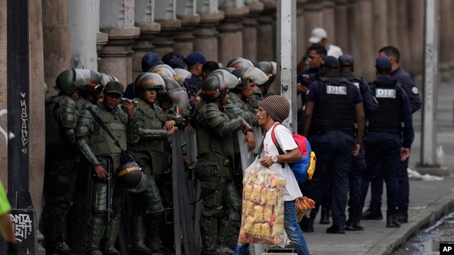 Un vendedor ambulante camina junto a miembros de la Guardia Nacional Bolivariana antes de la juramentación del presidente Nicolás Maduro para un tercer mandato, en Caracas, Venezuela, el domingo 5 de enero de 2025.