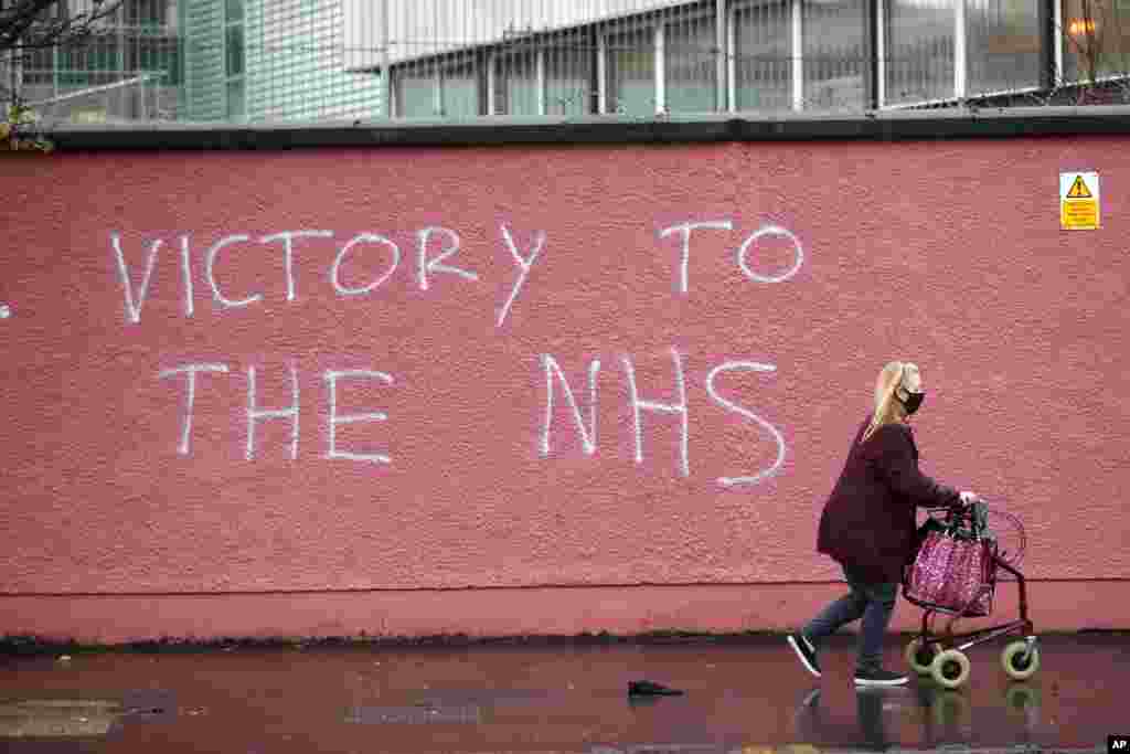 A woman walks past graffiti with the words Victory to the NHS (National Health Service) on a wall at the Royal Victoria Hospital.