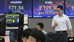 A currency trader passes by screens showing the Korea Composite Stock Price Index, right, and the foreign exchange rate at the foreign exchange dealing room of the KEB Hana Bank headquarters in Seoul, South Korea, June 3, 2020. 