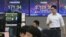 A currency trader passes by screens showing the Korea Composite Stock Price Index, right, and the foreign exchange rate at the foreign exchange dealing room of the KEB Hana Bank headquarters in Seoul, South Korea, June 3, 2020. 