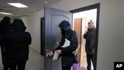 FILE - Police carry materials from the office of the Belarusian Association of Journalists as Andrei Bastunets, the group's leader, watches, in Minsk, Feb. 16, 2021. The association said Oct. 27, 2002, that journalist Ales Lyubyanchuk had been sentenced to three years in prison.