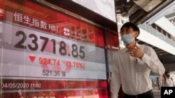 A man wearing face mask walks past a bank electronic board showing the Hong Kong share index at Hong Kong Stock Exchange Monday, May 4, 2020.
