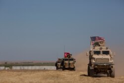 FILE - Turkish and American forces conduct their first joint ground patrol in the so-called "safe zone" on the Syrian side of the border with Turkey, seen in the background, near Tal Abyad, Syria, Sept. 8, 2019.