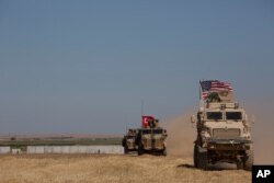 FILE - Turkish and American forces conduct their first joint ground patrol in the so-called "safe zone" on the Syrian side of the border with Turkey, seen in the background, near Tal Abyad, Syria, Sept. 8, 2019.