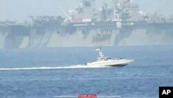 资料照片：伊朗革命卫队通过塔斯尼姆通讯社发布的照片显示一艘伊朗革命卫队快艇在波斯湾入口霍尔木兹海峡驶近美国海军“巴丹号”两栖攻击舰。(2023年8月20日)
