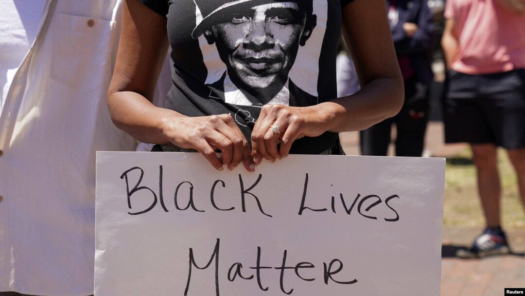 Seorang perempuan mengenakan kaus bergambar mantan presiden AS Barack Obama sambil memegang poster dalam unjuk rasa memprotes kematian pria Afrika-Amerika saat dalam pengawasan polisi. Unjuk rasa digelar dekat Gedung Putih, Washington D.C., 1 Juni 2020. (