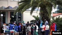 Migrants line up to receive sanitizers outside a hotel used as a refugee shelter, after authorities found several cases of the novel coronavirus and put the area under quarantine, in Kranidi, Greece, April 21, 2020.