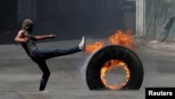 A Palestinian protester rolls a burning tire during clashes with Israeli troops in Hebron in the occupied West Bank, July 27, 2018. On Tuesday, Israeli security forces arrested a prominent Palestinian writer in Hebron.