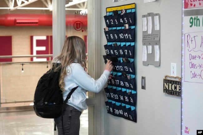 FILE - A ninth-grader places her phone in a holder as she enters class at Delta (Utah) High School, Feb. 23, 2024. Many schools try to regulate student cellphone use, but kids don’t always follow the rules and schools enforce them sporadically.