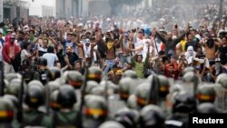 Para pendukung tokoh oposisi Henrique Capriles berhadap-hadapan dengan polisi anti huru-hara di Caracas (15/4). Ratusan pendukung oposisi bentrok dengan petugas keamanan Senin 16/4. 