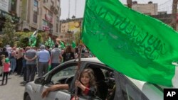 Seorang gadis Palestina melihat keluar dari kendaraan keluarganya dan mengibarkan bendera hijau Hamas di kota Ramallah, Tepi Barat, 21 Mei 2021. (Foto: AP/Nasser Nasser)