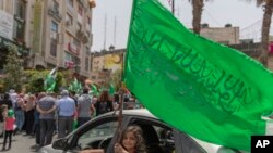 Seorang gadis Palestina melihat keluar dari kendaraan keluarganya dan mengibarkan bendera hijau Hamas di kota Ramallah, Tepi Barat, Jumat, 21 Mei 2021. (Foto: AP)