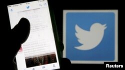 FILE - A man reads tweets on his phone in front of a displayed Twitter logo in Bordeaux, southwestern France.