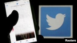 FILE - A man reads tweets on his phone in front of a displayed Twitter logo in Bordeaux, southwestern France.