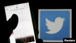 FILE - A man reads tweets on his phone in front of a displayed Twitter logo in Bordeaux, southwestern France.