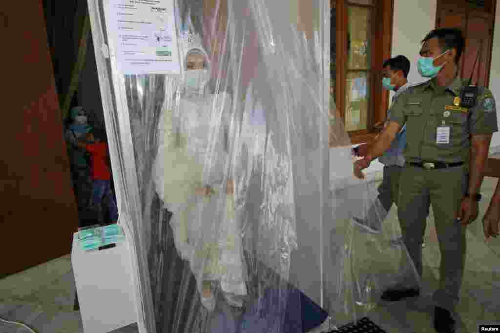 Seorang pengantin perempuan mengenakan masker disemprot di dalam ruang disinfeksi pada hari pernikahannya di Surabaya, Jawa Timur (foto: Antara/Reuters).