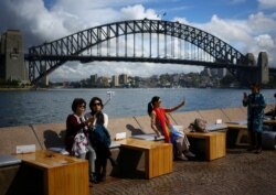 FILE - Tourists take photographs with their mobile phones in front of the Sydney Harbor Bridge, in Sydney, Australia, Oct. 13, 2018.