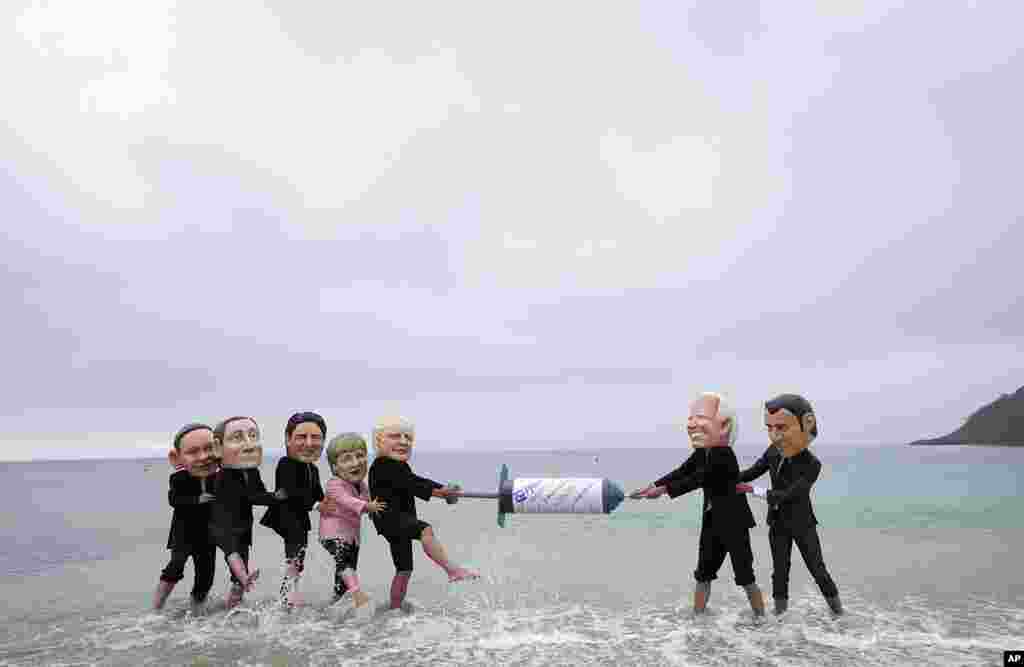 Activists wearing giant heads of the G7 leaders tussle over a giant COVID-19 vaccine syringe during an action of NGO&#39;s on Swanpool Beach in Falmouth, Cornwall, England.