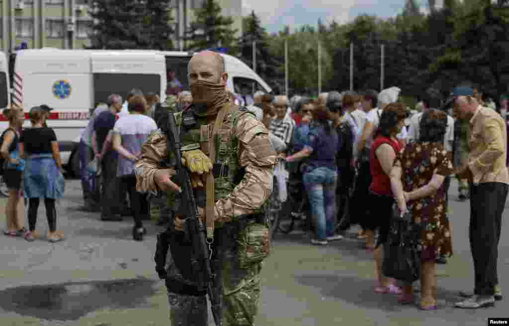 An armed man stands guard as people wait for humanitarian medical aid near the mayor's office in Slovyansk, Ukraine, July 9, 2014.