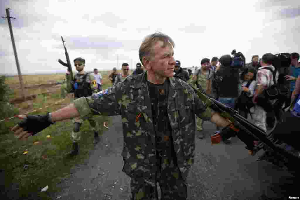 An armed pro-Russian separatist stands guard as OSCE monitors and a team of Malaysian air crash investigators inspect the crash site of Malaysia Airlines Flight MH17, near Hrabove, Ukraine, July 22, 2014. 