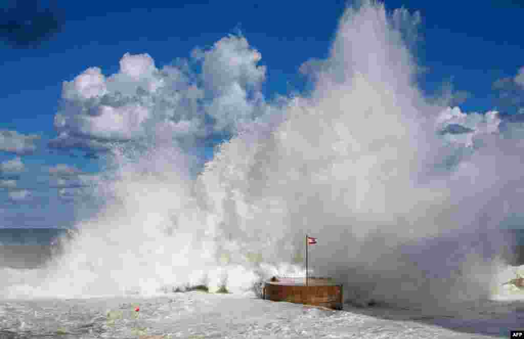 The Lebanese national flag flutters on a dyke as waves crash on the shores of Beirut promenade of al-Manara.