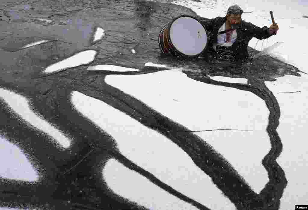 Um búlgaro quebra o gelo à medida que tenta atravessar o rio de Tundzha, à sua frente outros cantam e dançam em celebração do Dia da Epifania na cidade de Kalofer. Jan 6, 2015. Bulgária. &nbsp;