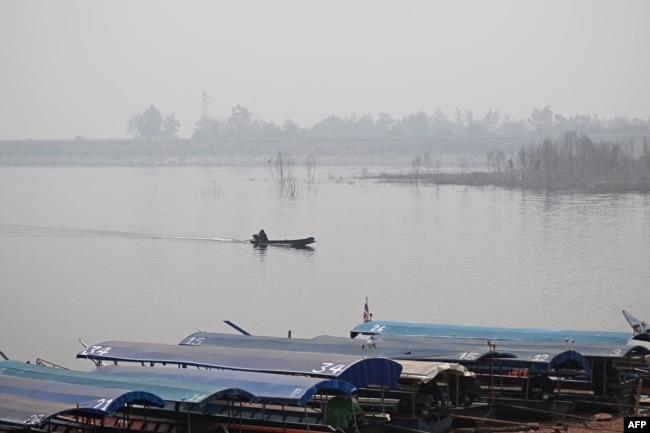 A man steers a boat on a lake amidst high air pollution at the Srilanna National Park in the northern Thai province of Chiang Mai on March 16, 2024. (Photo by Lillian SUWANRUMPHA / AFP)