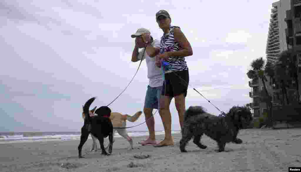 Bob Jenkins memegang topinya saat bersama kawannya Darlene Pittman membawa anjing mereka berjalan-jalan di tengah angin dari Badai Arthur yang semakin kencang di Pantai Surfside, South Carolina (3/7).&nbsp;(Reuters/Randall Hill)