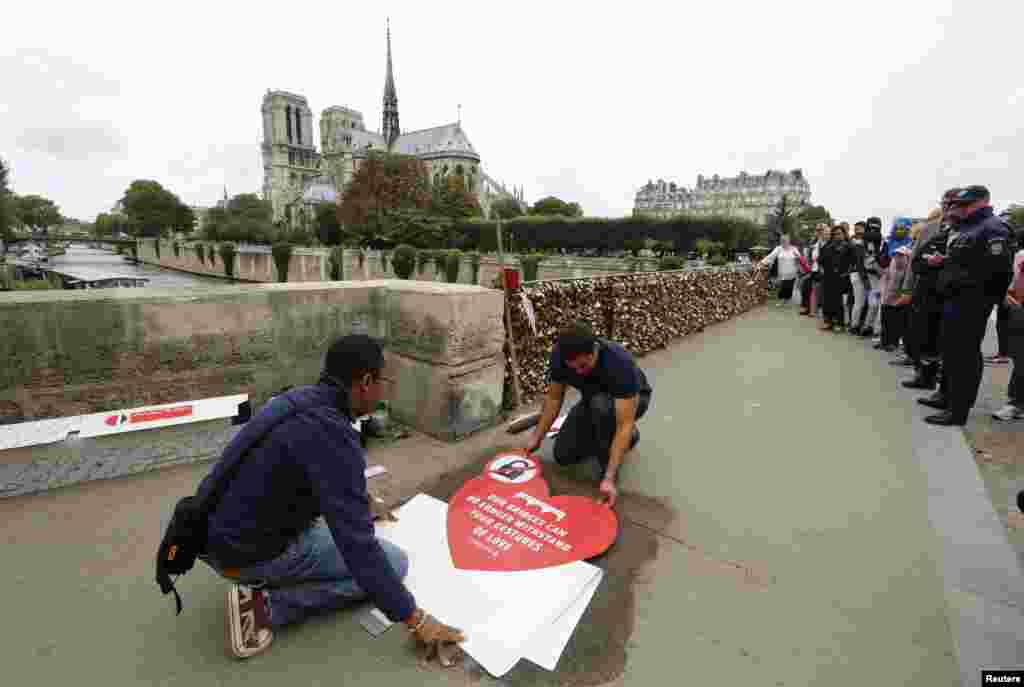 Công nhân đặt một tấm bảng với thông điệp "Những cây cầu của chúng tôi không còn có thể chịu được những cử chỉ tình yêu của bạn" trên vỉa hè cây cầu Pont de l'Archeveche, gần Nhà thờ Đức Bà. Cây cầu được gắn hàng ngàn những ổ khóa, gọi là ổ khóa tình yêu tại Paris, Pháp. 