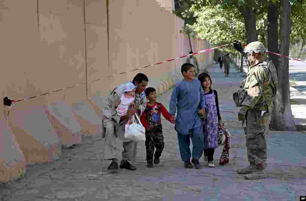 A U.S. military force helps an Afghan family walk past the site of a suicide attack near a U.S. military camp in Kabul, Sept. 16, 2014.