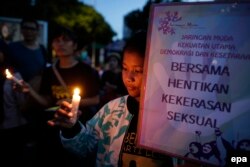 Seorang remaja memegang lilin dan poster bertuliskan “Bersama, hentikan kekerasan seksual,” dalam doa bersama untuk seorang korban kekerasan seksual berusia 14 tahun, yang digelar di depan istana kepresidenan, Jakarta, 4 Mei 2016.