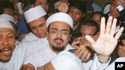 ນັກສອນສາສະໜາ ອິສລາມ ຫົວຮຸນແຮງ Habib Rizieq (ກາງ) ພະຍາຍາມຂໍໃຫ້ພວກສະໜັບສະໜູນ ທີ່ສະຫງົບ ໃນຂະນະທີ່ເຂົາເຈົ້າກຳລັງຖືກຄວບຄຸມຕົວ ອອກໄປຈາກ ຫ້ອງການສານ ໃນນະຄອນຫຼວງ Jakarta, ວັນທີ 21 ເມສາ 2003.