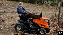 In this photo provided by Ed Smith, Geoffrey Holt rests his leg on top of his riding mower in Hinsdale, N.H., on April 4, 2020. Holt left the town of Hinsdale nearly $4 million when he died last June. (Ed Smith via AP)