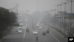 Seorang perempuan India menyeberang jalan raya saat kendaraan bergerak dalam kabut akibat polusi di New Delhi, India (15/1). 