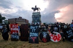 FILE - Protesters with shields and gas masks wait for police action as they surround the statue of Confederate Gen. Robert E. Lee on Monument Avenue in Richmond, Va., on June 23, 2020.