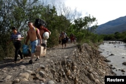 FILE - Venezuelans carry their belongings along a pathway after illegally entering Colombia through the Tachira river close to the Simon Bolivar International bridge in Villa del Rosario, Colombia, Aug. 25, 2018.