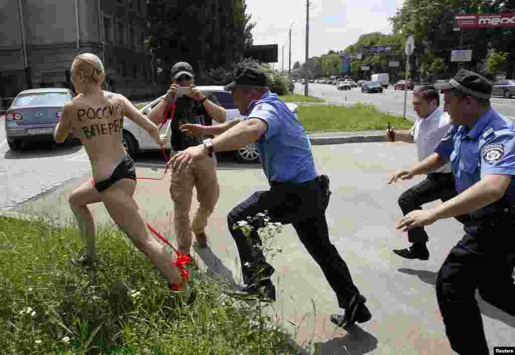 Nhân viên công lực Ukraina ở Kiev đuổi theo một phụ nữ thuộc phong trào đòi nữ quyền FEMEN biểu tình bên ngoài Sứ quán Nga để phản ứng trước vụ Tổng thống Putin loan báo li dị bà vợ. Hàng chữ trên lưng có nghĩa là “Đẩy nước Nga tiến tới.” 