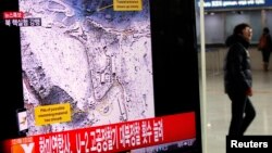 一名旅客2013年2月12日在首爾的一個火車站經過一個正在播放朝鮮核試驗的電視看版。