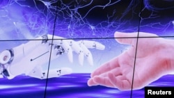 FILE PHOTO: An illustration projected on a screen shows a robot hand and a human one moving towards each others during the "AI for Good" Global Summit at the ITU in Geneva
