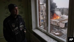 A local resident stands at the window as smoke raises from the burning building after the Russian shelling in the town of Chasiv Yar, the site of the heaviest battles with the Russian troops, Donetsk region, Ukraine, Feb. 27, 2023. 