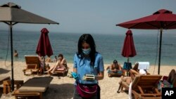 An employee of a beach bar, wearing a protective mask against the coronavirus, collects money for sunbed rentals, at Alimos beach, near Athens, Saturday, May 16, 2020. 