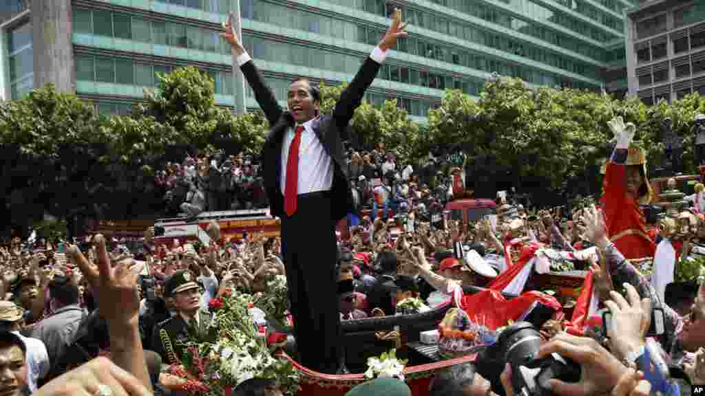 Presiden Joko Widodo mengacungkan salam tiga jari pada kerumunan rakyat dalam parade jalanan menyusul pelantikannya di Jakarta (20/10). (AP/Achmad Ibrahim)
