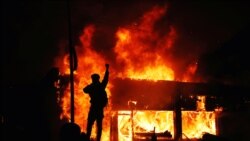 A protester gestures as buildings burn during continued demonstrations against the death in Minneapolis police custody of African-American man George Floyd, in Minneapolis, Minnesota, U.S., May 30, 2020.
