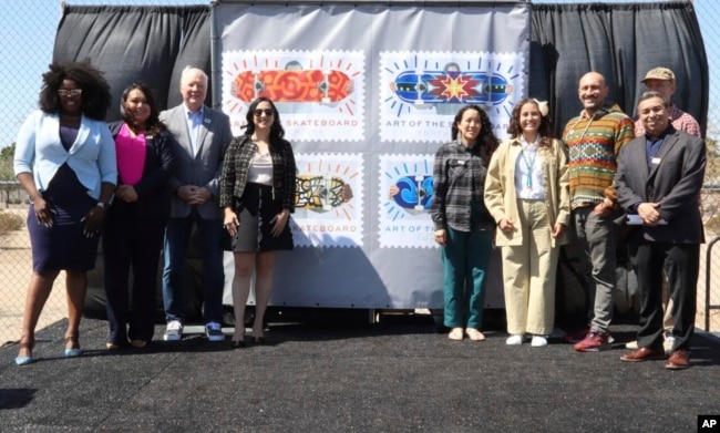 In this image provided by the U.S. Postal Service, USPS officials and artists who contributed to new skateboarding themed stamps pose in front of a display of the "Art of the Skateboard" Forever stamps in Phoenix, Friday, March 24, 2023. (Rod Spurgeon/U.S. Postal Service via AP)