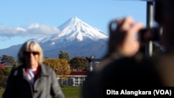 FILE - A man takes a picture of his wife with Mount Taranaki, also known as Mount Egmont, in the background in New Plymouth, New Zealand, Sept. 26, 2011. (AP Photo/Dita Alangkara, File)