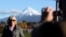 FILE - A man takes a picture of his wife with Mount Taranaki, also known as Mount Egmont, in the background in New Plymouth, New Zealand, Sept. 26, 2011. (AP Photo/Dita Alangkara, File)