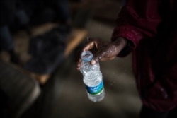 FILE - An African migrant fills an empty bottle with leaking water from the roof of a barrack in a detention center for illegal migrants in Abu Salim district on the outskirts of Tripoli, LIbya, Nov. 29, 2013.